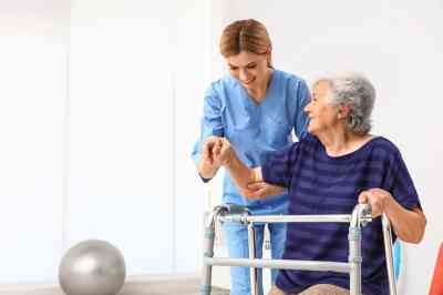 Pflegekraft hilft älterer Frau mit Gehhilfe